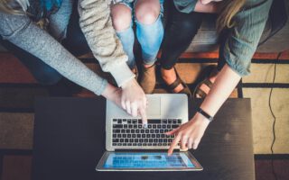 3 Menschen von oben die einen Computer nutzen
