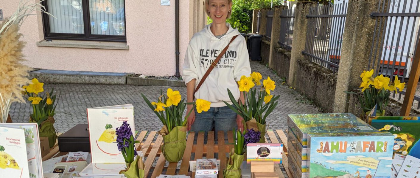 Frau an Marktstand mit Büchern, Flyern, Spielen und mehr.