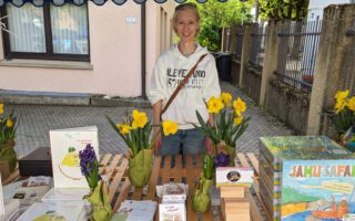 Frau an Marktstand mit Büchern, Flyern, Spielen und mehr.