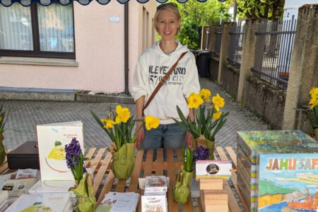 Frau an Marktstand mit Büchern, Flyern, Spielen und mehr.
