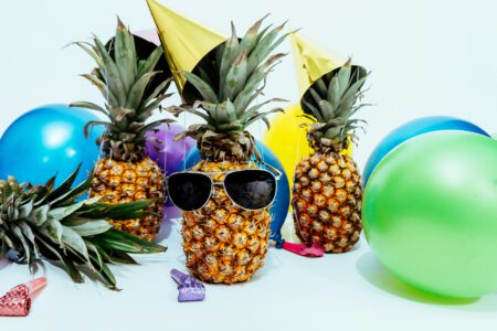 Ananas zwischen Luftballons mit Partyhüten und Sonnenbrille