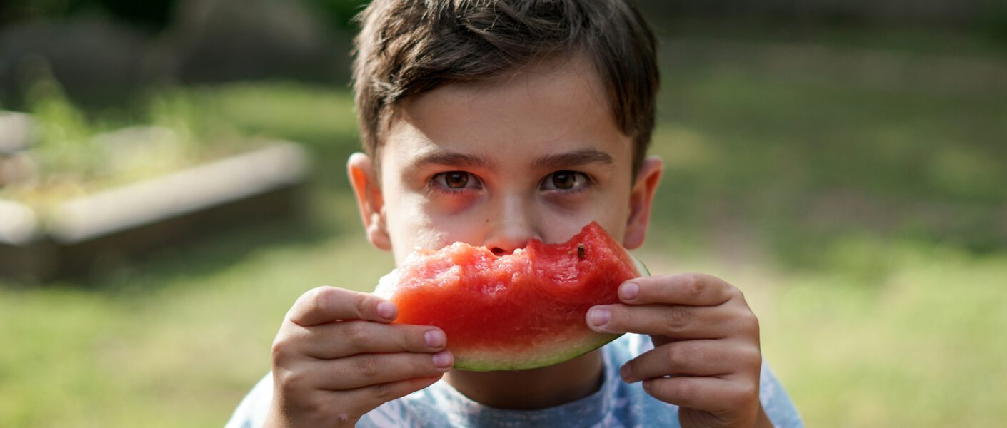 Junge hält angebissene Melone hin.