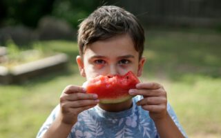 Junge hält angebissene Melone hin.