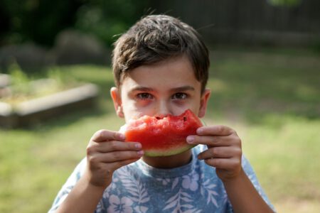 Junge hält angebissene Melone hin.