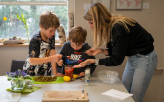Frau kocht mit zwei Kindern am Tisch.